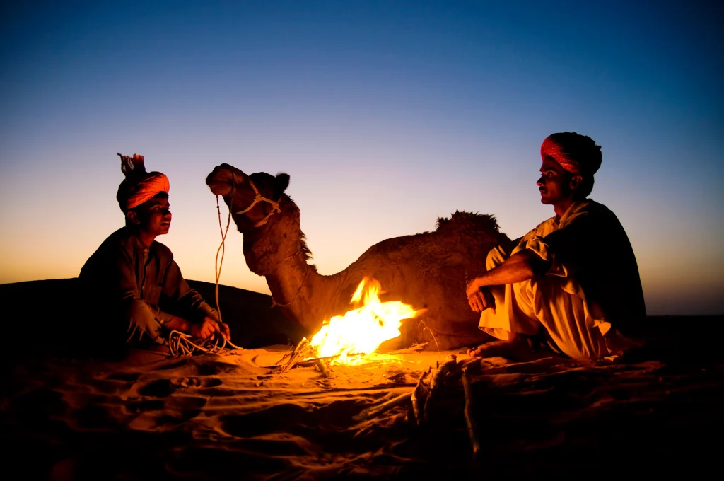 Hommes indiens se reposant près d'un feu de camp avec leur chameau