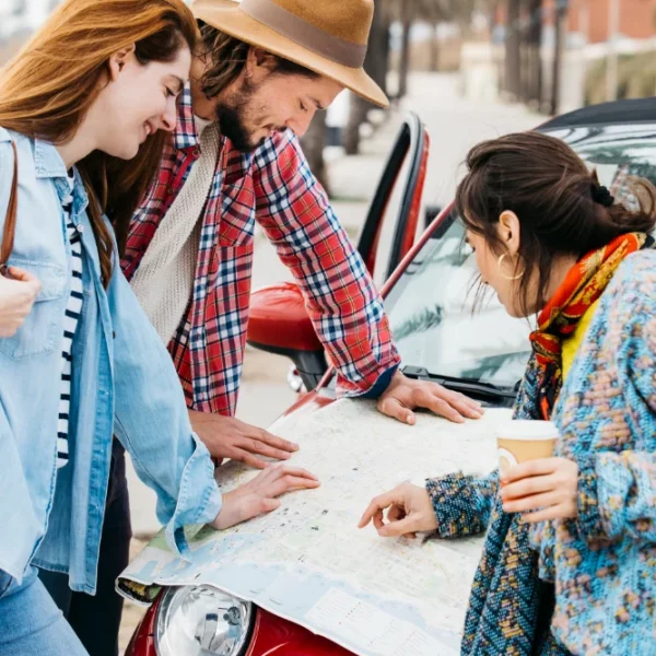 People looking at a road map near a red car