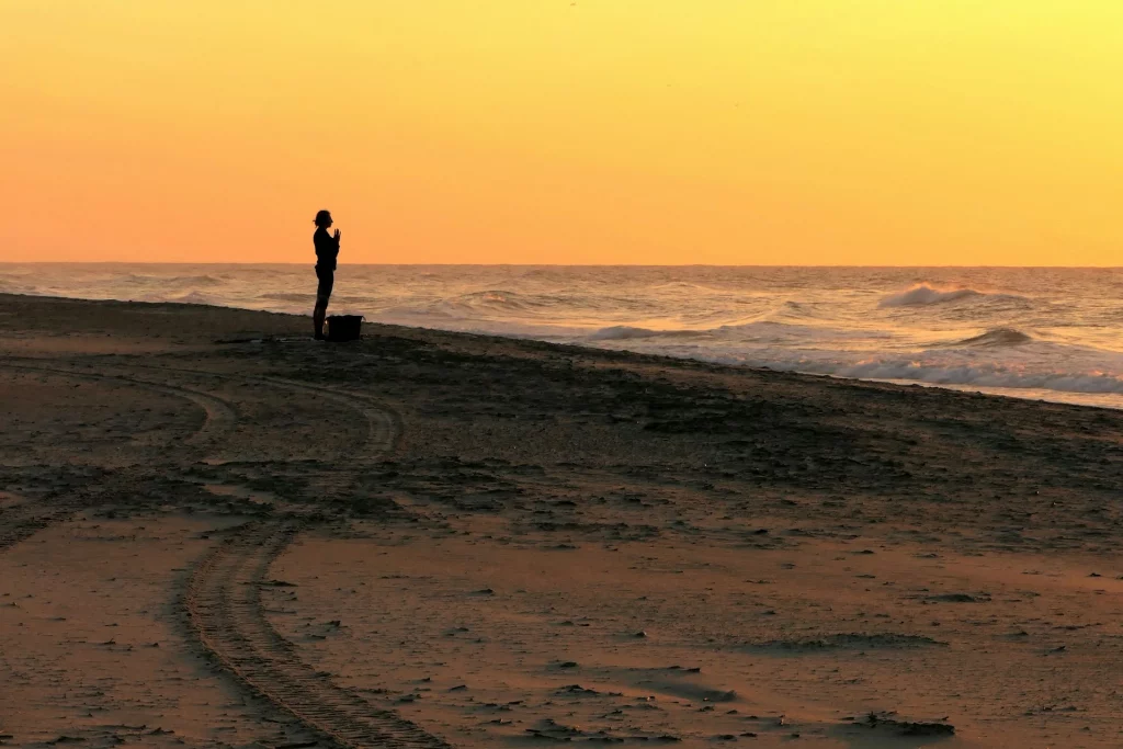 Silhouette d'une personne méditant sur une plage déserte au coucher du soleil