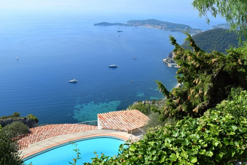 Piscine à débordement avec vue panoramique sur la mer Méditerranée, entourée de verdure et baignée de lumière naturelle.