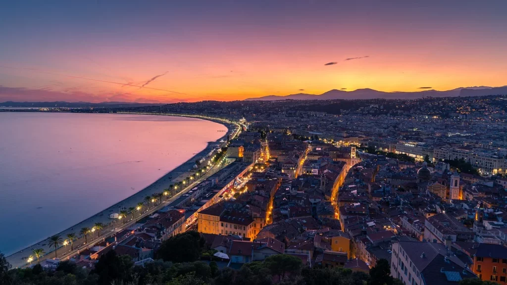 Plage ensoleillée à Nice, avec des eaux turquoise et des montagnes en arrière-plan, typiques de la Côte d'Azur.